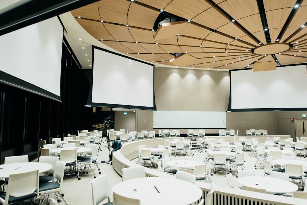 A conference room set with round tables and large presentation screens