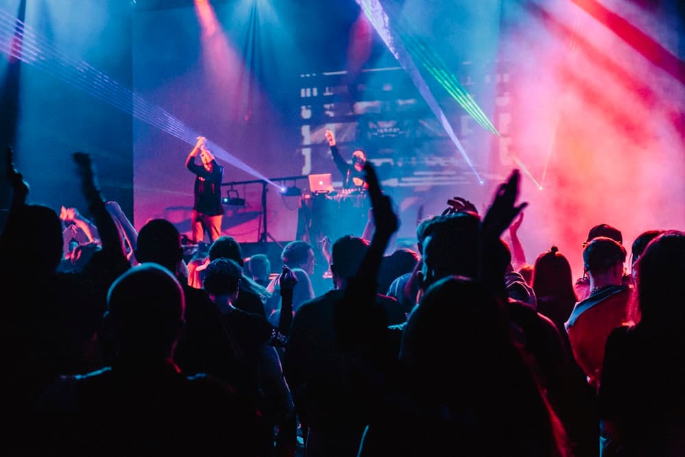 A crowd with hands raised in front of a lit stage at a live music event