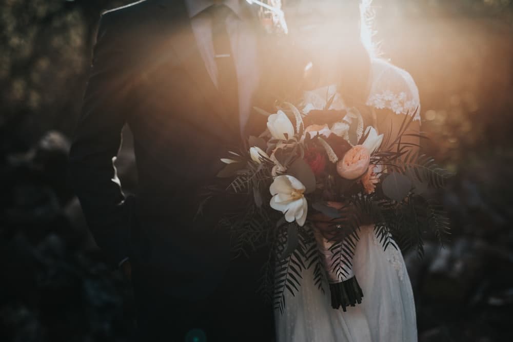 A couple at a wedding, the bride holding a bouquet in warm evening light